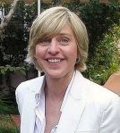 Smiling person in white blazer outdoors.