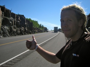 Person hitchhiking on a sunny roadside.
