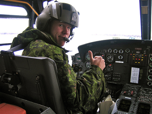 A man in camouflage sitting inside of an airplane.