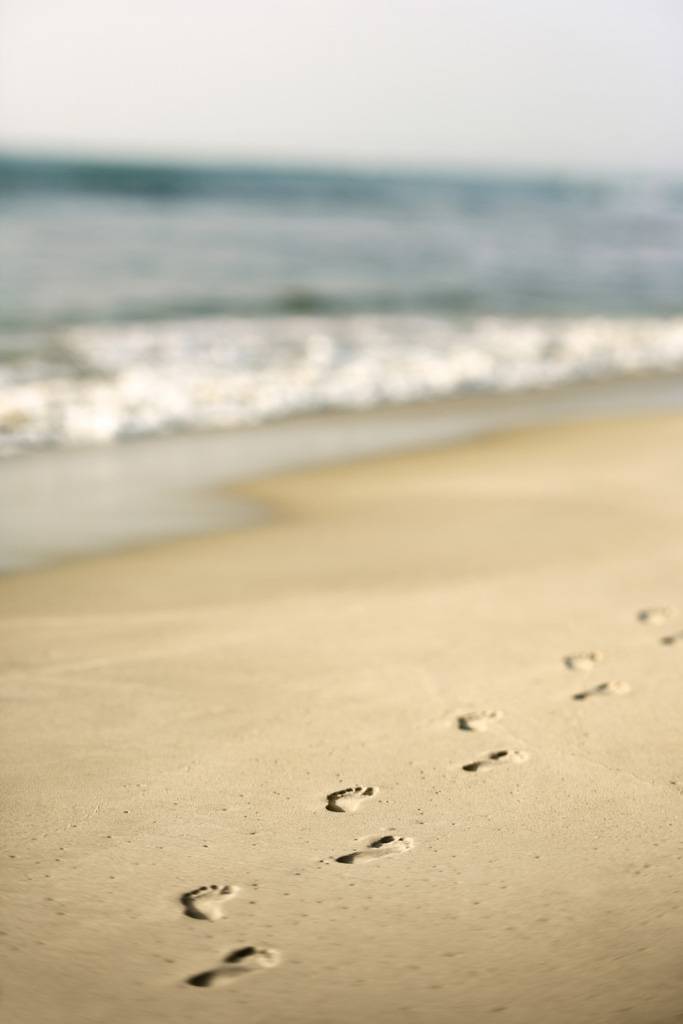 A beach with footprints in the sand and waves